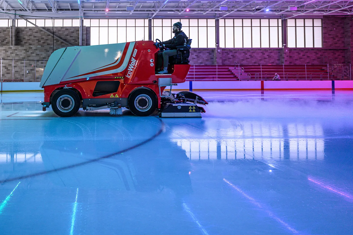 An ice technician, drives the electric Engo IceWolf ice resurfacing machine amidst colorful light at the Sub-Zero Ice Center in the Bakke Recreation & Wellbeing Center